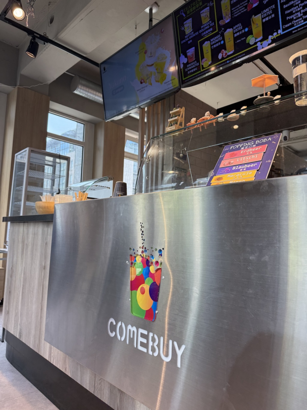 Innenansicht eines Comebuy-Bubble-Tea-Shops: Theke mit Comebuy-Logo, darüber digitale Menübildschirme und eine Karte mit Popping-Boba-Sorten.