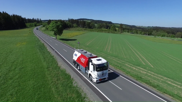Luftaufnahme eines roten und weißen Tanklastwagens auf einer Landstraße, umgeben von grünen Feldern und Wäldern unter blauem Himmel
