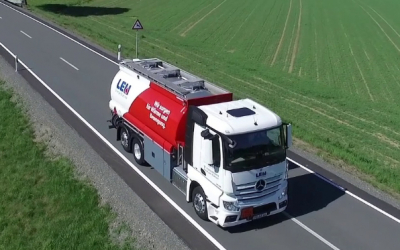 Luftaufnahme eines roten und weißen LEU-Tanklastwagens auf einer Landstraße neben grünen Feldern