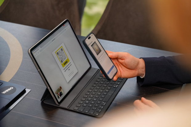 Person hält ein Smartphone vor ein Tablet mit eingeblendetem Wero-QR-Code, um eine Zahlung per Scan zu starten.