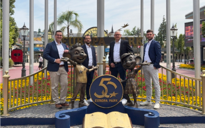 Vier Männer stehen vor dem Eingang des Europa-Park neben zwei Maskottchen-Figuren und einem ‚50 Jahre Europa-Park‘-Schild, im Hintergrund Blumenbeete und Parkkulisse