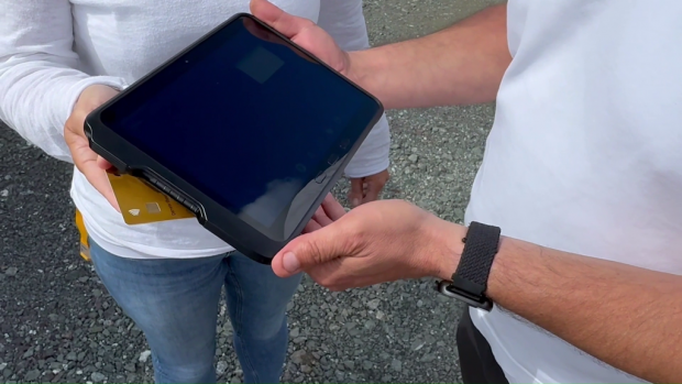 Zwei Personen halten ein Tablet im Outdoor-Einsatz; eine kontaktlose Bankkarte wird daneben gezeigt, der Bildschirm ist dunkel.